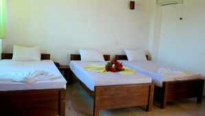 Una habitación de hotel con dos camas individuales, un cabecero de madera, una mesita con un ramo de flores y un equipo de aire acondicionado en la pared.