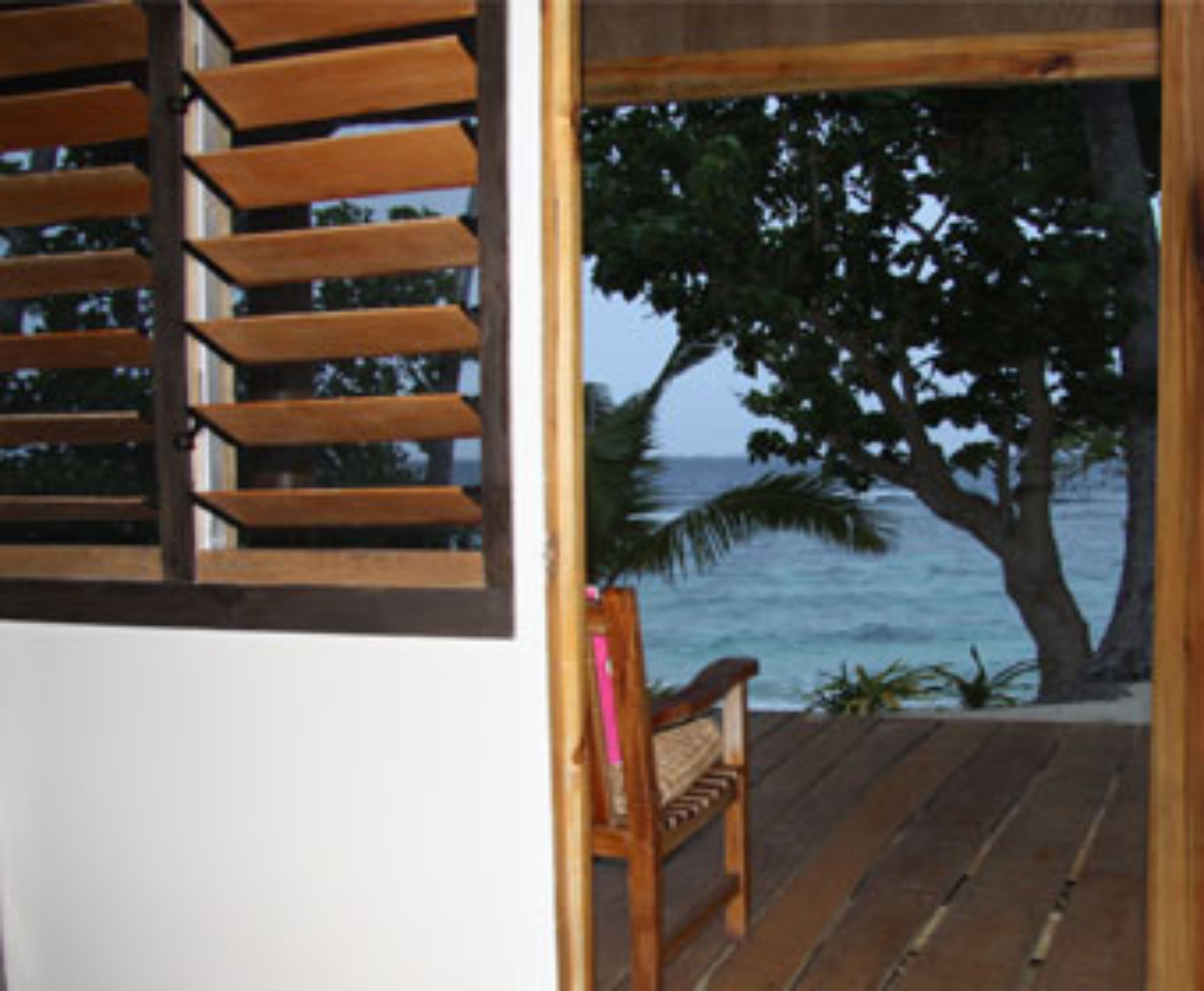 A wooden bench on a deck with a view of the ocean and a tree.