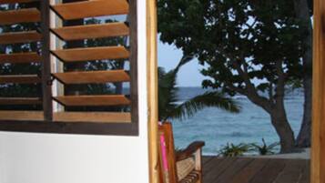 A wooden bench on a deck with a view of the ocean and a tree.