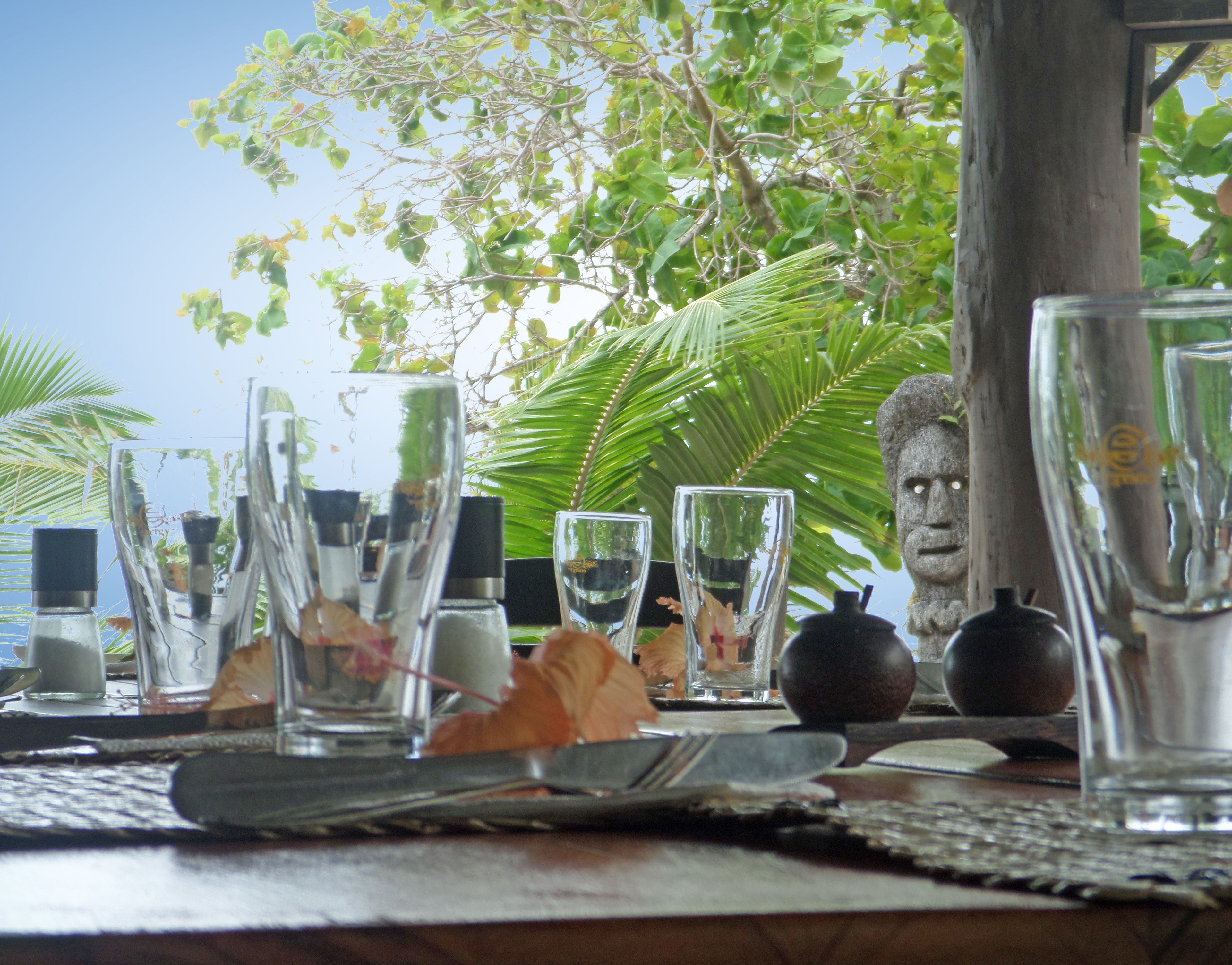 A table set with clear glasses, a knife, and a fruit, with a tropical backdrop.