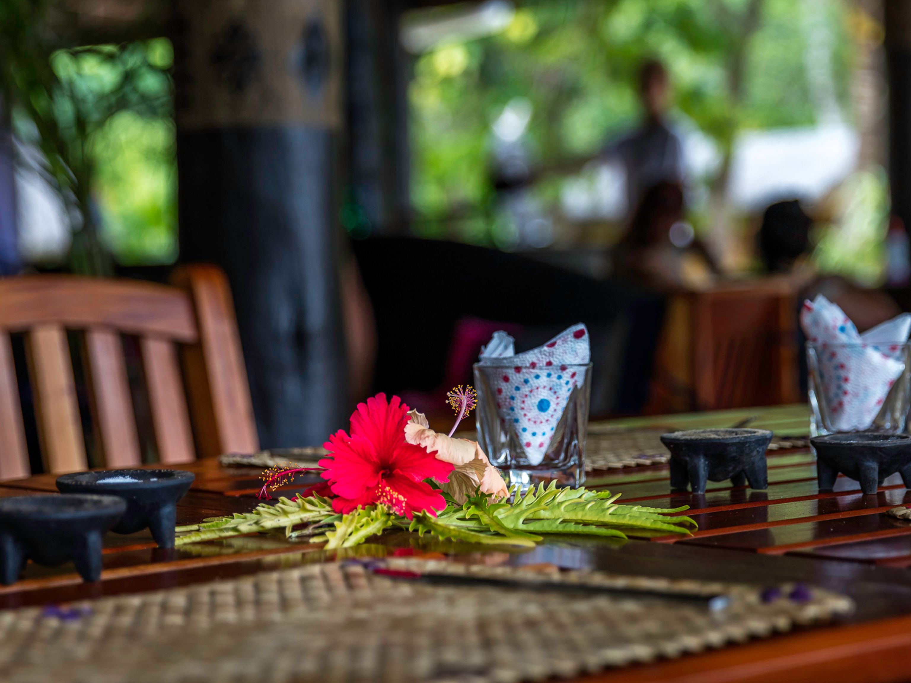 A dining table with a red flower centerpiece, patterned napkins, and small black candle holders.