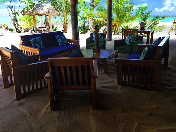 Un área de estar junto a la playa con muebles de madera y una estructura de techo de paja.