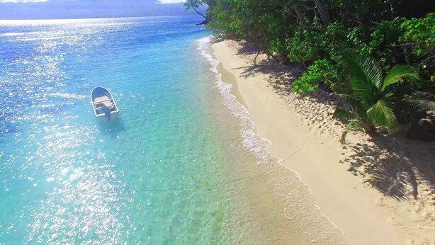 Un bateau sur une mer turquoise aux eaux limpides, une plage de sable et une végétation luxuriante.