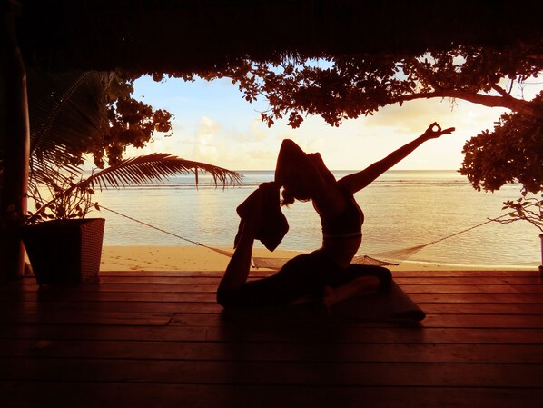 A person performing a yoga pose on a wooden deck with a view of the ocean and palm trees.