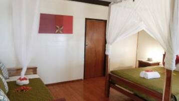 Una habitación con cama, piso de madera, puerta y un cuadro colgado en la pared.