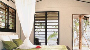 Un lit recouvert d’une couvre-lit à motifs verts, avec des oreillers blancs et un ciel de lit blanc.