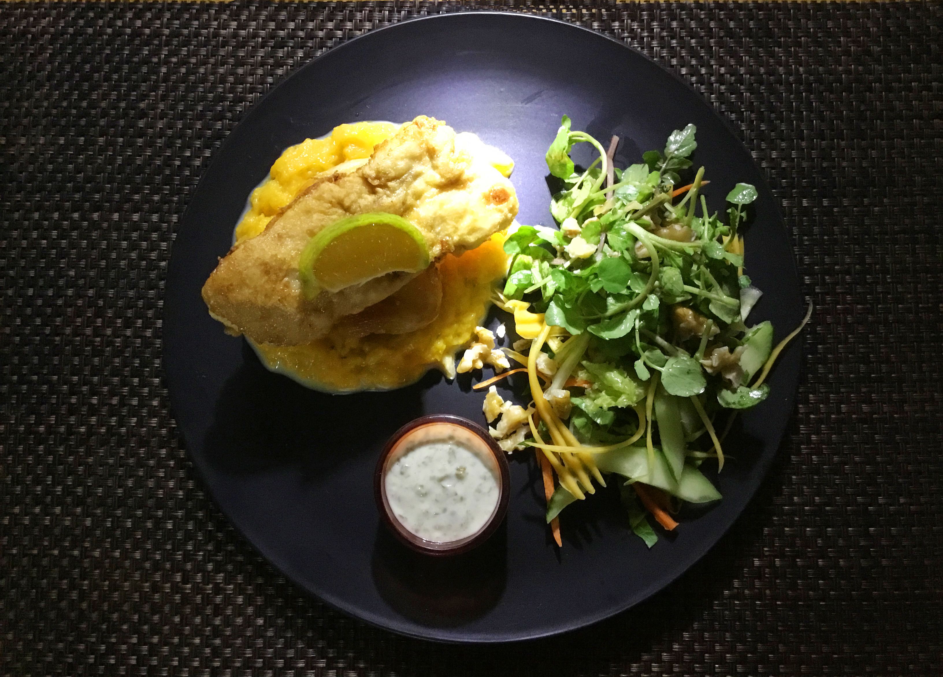 Une assiette comprenant un plat frit, une salade en accompagnement et un petit bol de sauce.