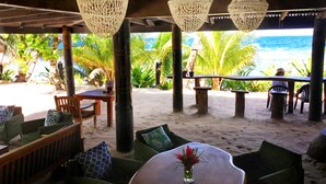 Un espace aménagé près de la plage, avec une table, des chaises et des lampes suspendues.