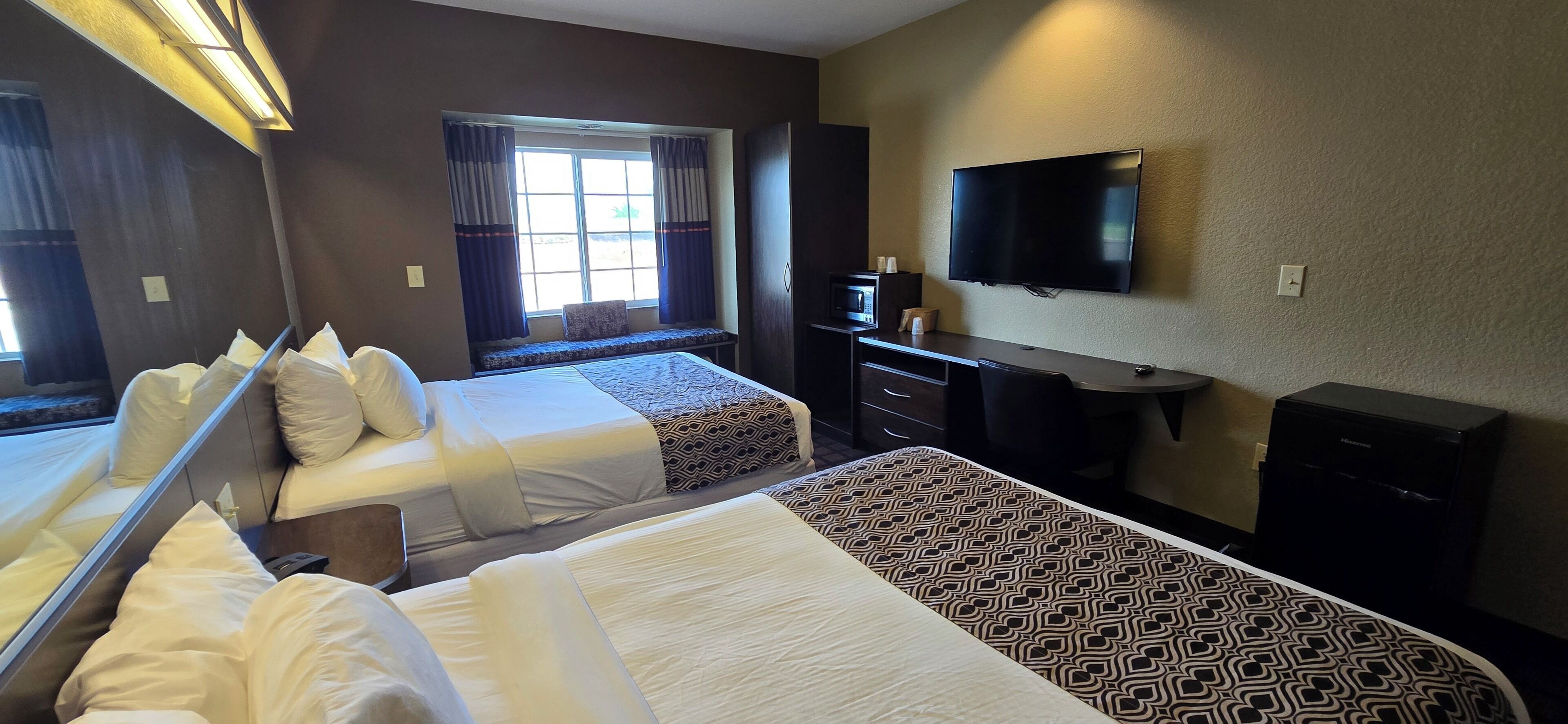 A hotel room with two beds, a desk, a television, and a window with curtains.