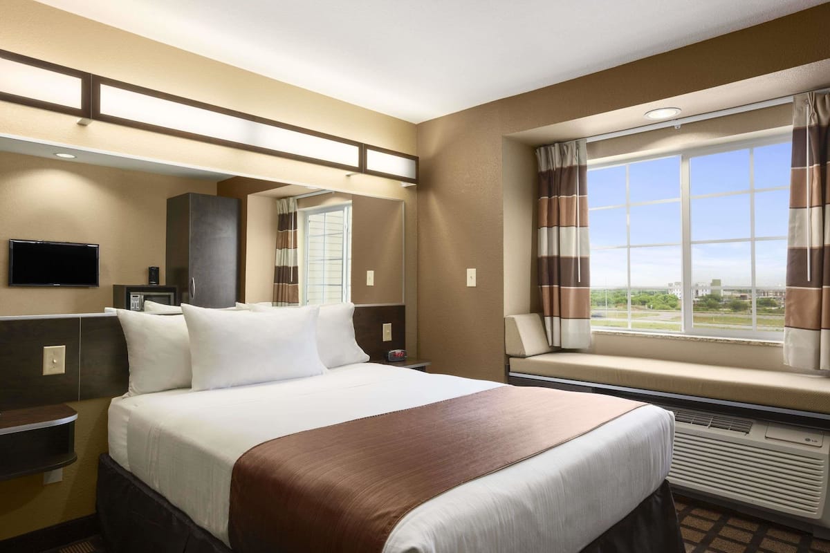 Une chambre d’hôtel avec un grand lit, une télévision, un miroir, une fenêtre avec des rideaux et une vue sur l’extérieur.