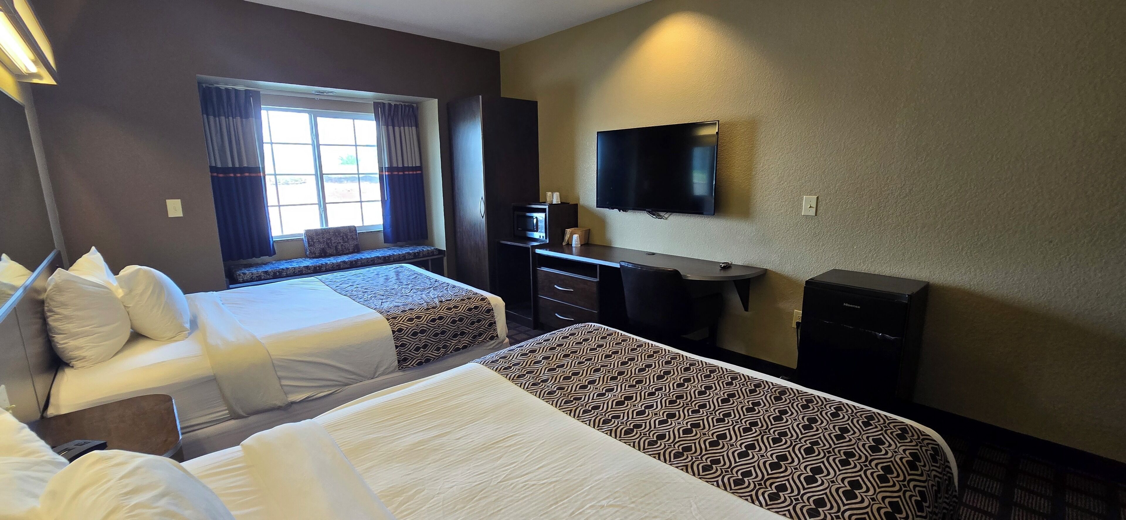 A hotel room with two beds, a TV, a desk with a chair, and a window with curtains.