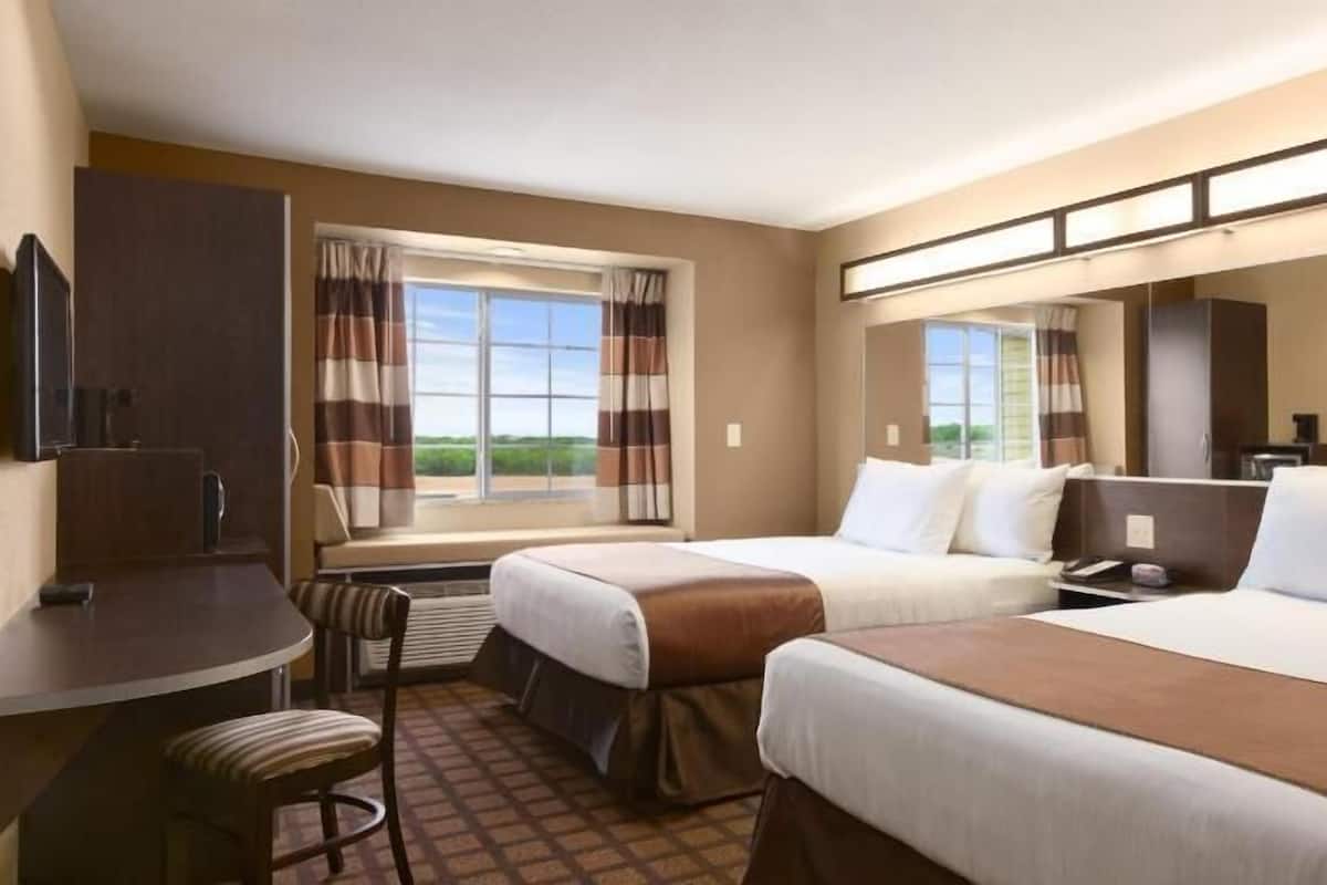 Une chambre d’hôtel avec deux lits, un bureau, une chaise, une télévision et de grandes fenêtres avec des rideaux.