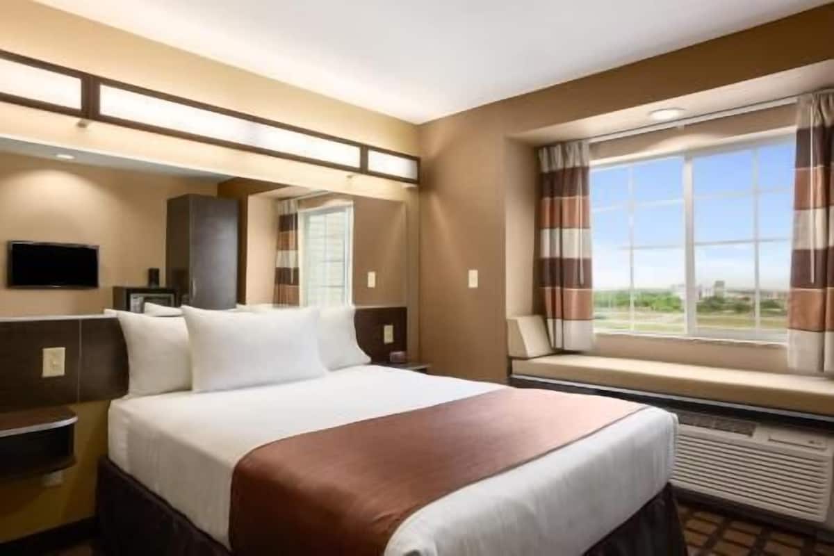 Une chambre d’hôtel avec un grand lit, un téléviseur fixé au mur, une fenêtre avec des rideaux et une vue sur l’extérieur.