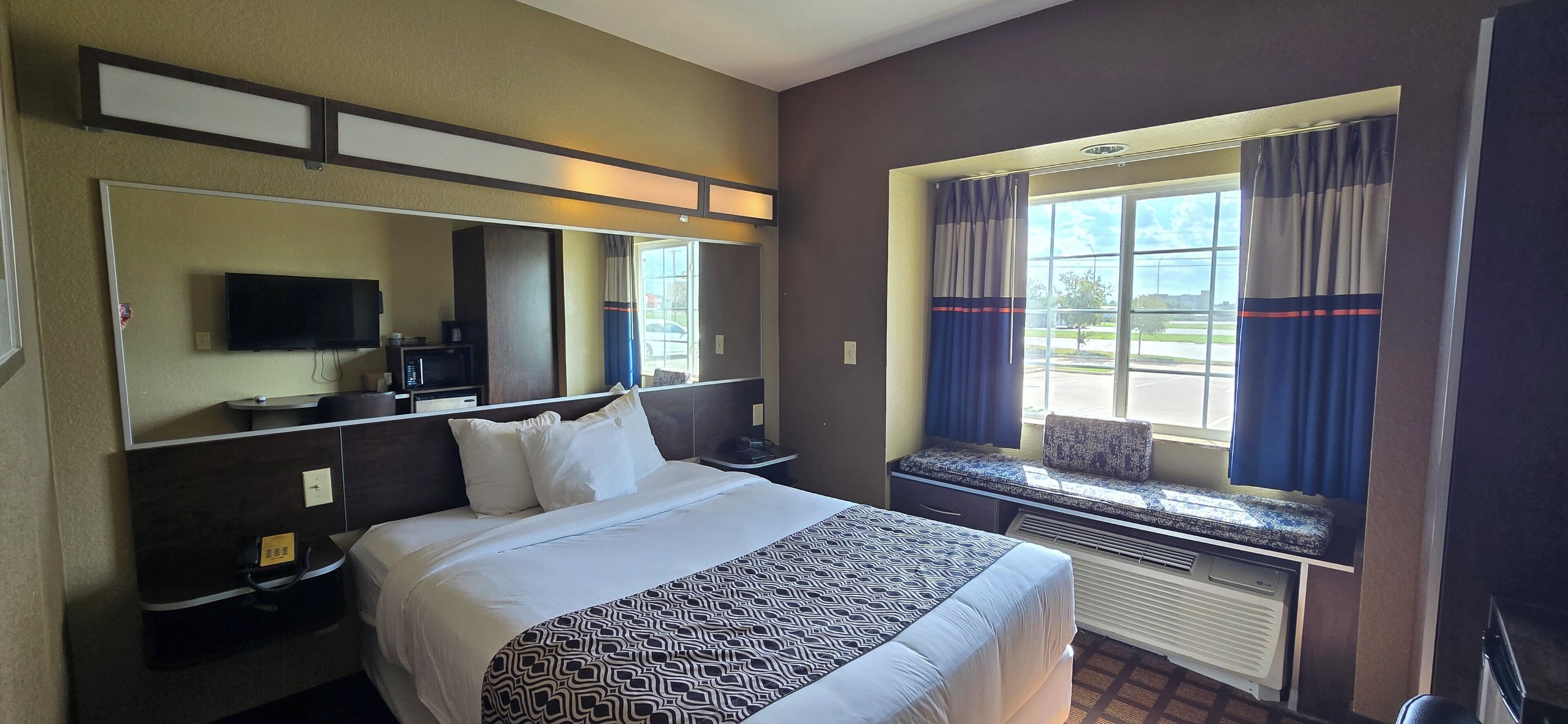 A hotel room with a large bed, a flat-screen TV, a microwave, a small table, and a window with curtains.