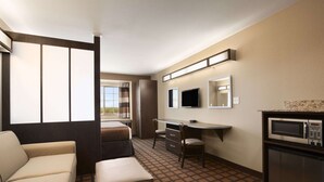 Ein Hotelzimmer mit einer Couch, einem Schreibtisch, einem Fernseher, einer Mikrowelle und einem Fenster mit Vorhängen.