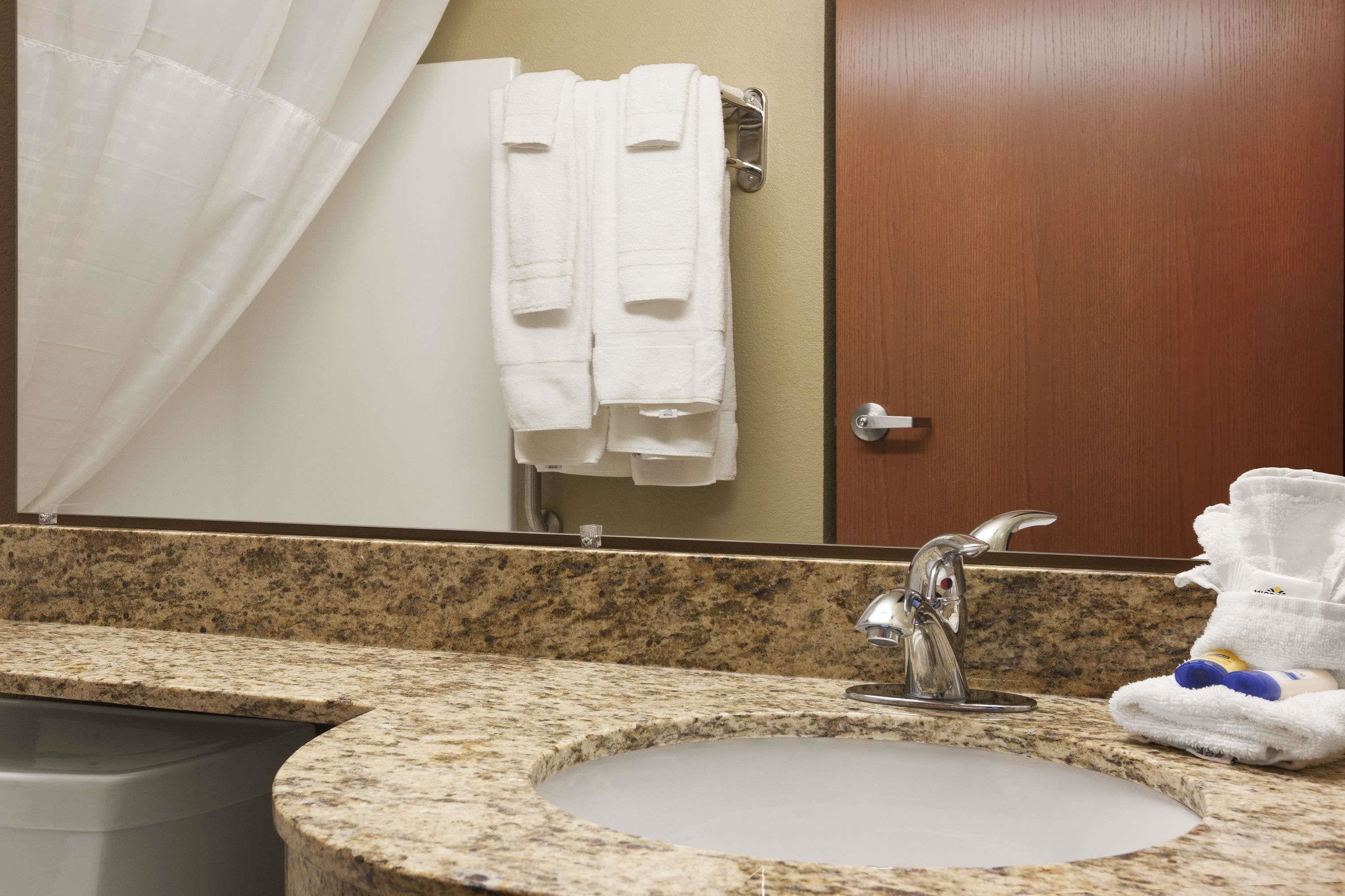 A bathroom with a granite countertop sink, a mirror, a towel rack with two white towels, and a wooden door.