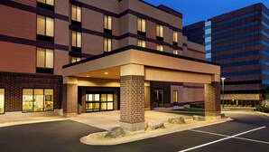 Un hotel de varios pisos con vestíbulo cubierto, amplias ventanas y estacionamiento.