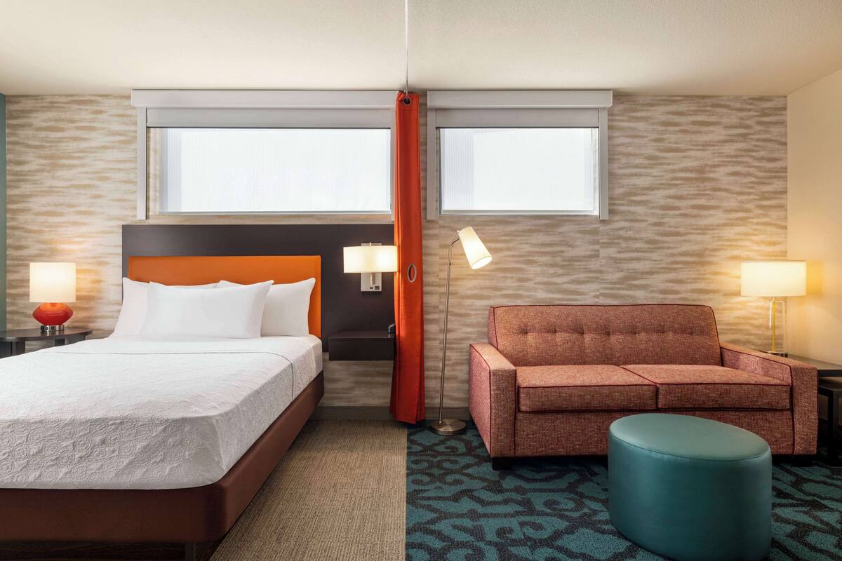 Una habitación de hotel con una cama grande, un sofá, un reposapiés y dos lámparas.