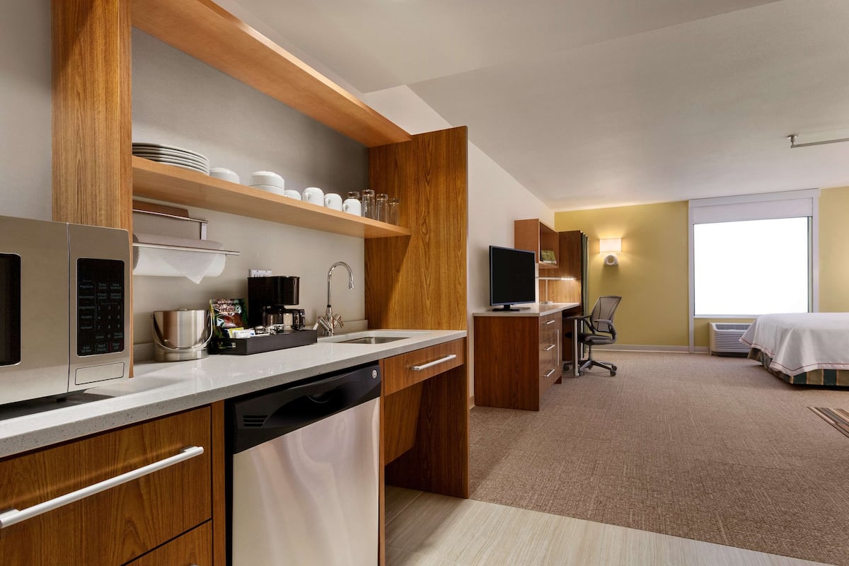 Una habitación de hotel moderna con kitchenette, una cama, un escritorio y un ventanal grande.