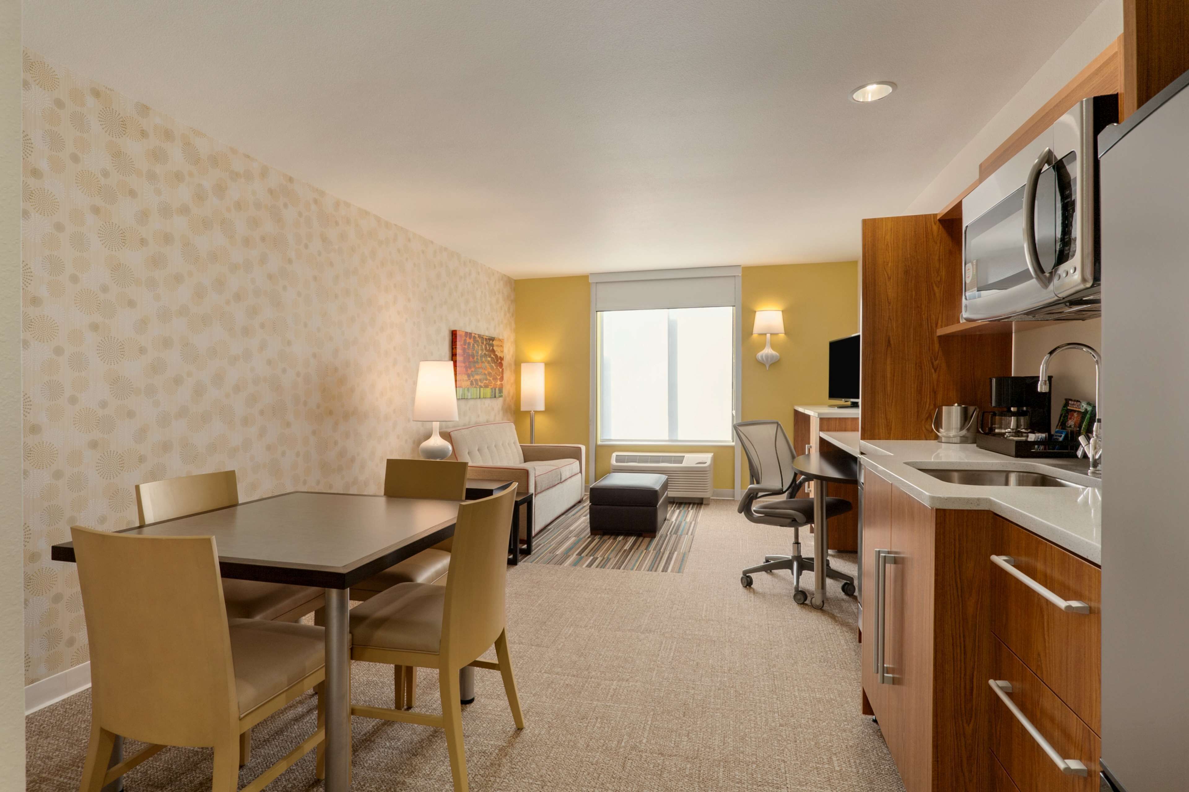 Habitación de hotel compacta con zona de comedor, kitchenette y un amplio ventanal.