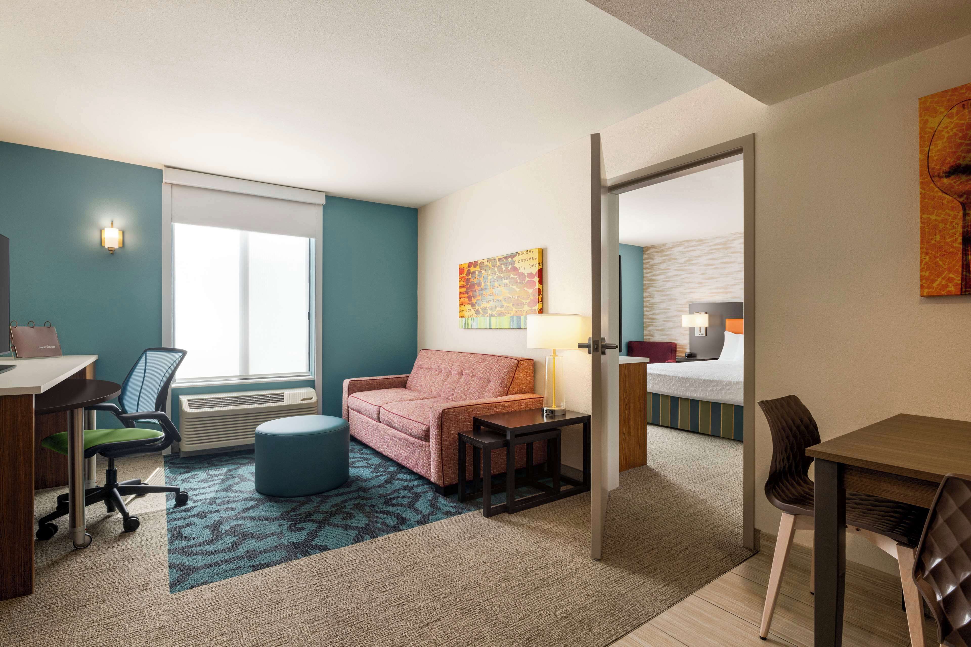 Habitación de hotel con escritorio, sofá, mesita, silla, lámpara y cama.
