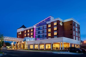 A multi-story hotel with a prominent entrance, a covered parking area, and a well-lit facade.