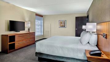 A hotel room with a large bed, a TV, a desk with drawers, a lamp, and a bedside table with a phone.