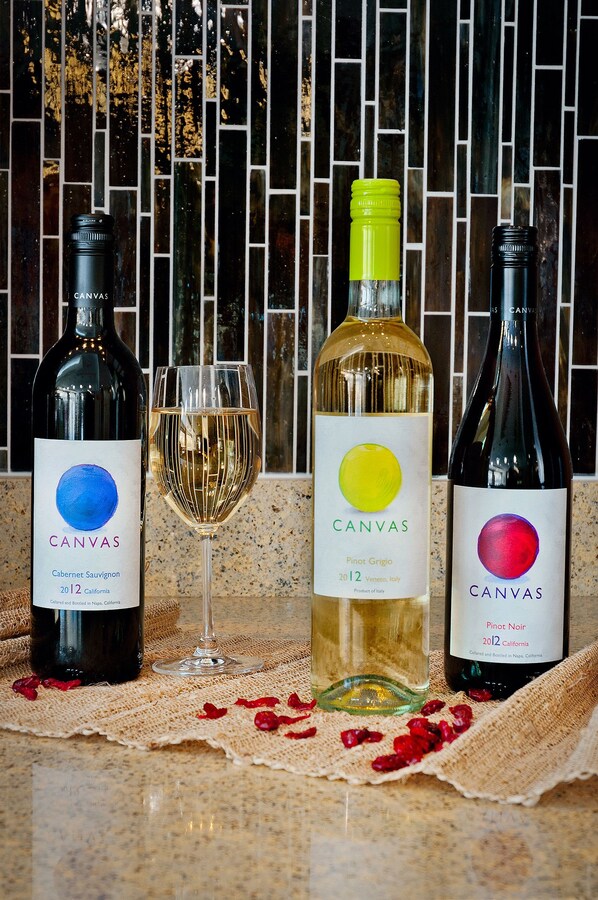Three bottles of wine and a wine glass on a table with a mosaic tile backsplash.
