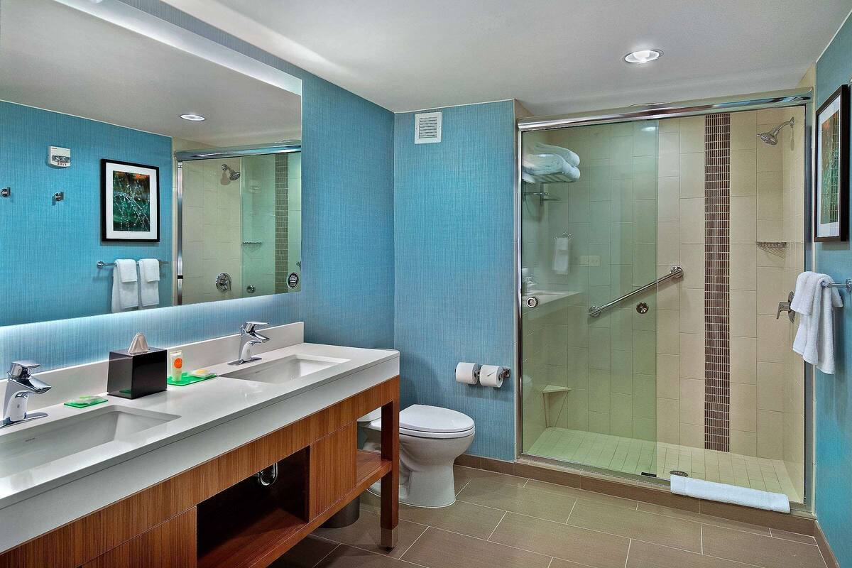 A modern bathroom with a large mirror, two sinks, a toilet, and a glass-enclosed shower area.