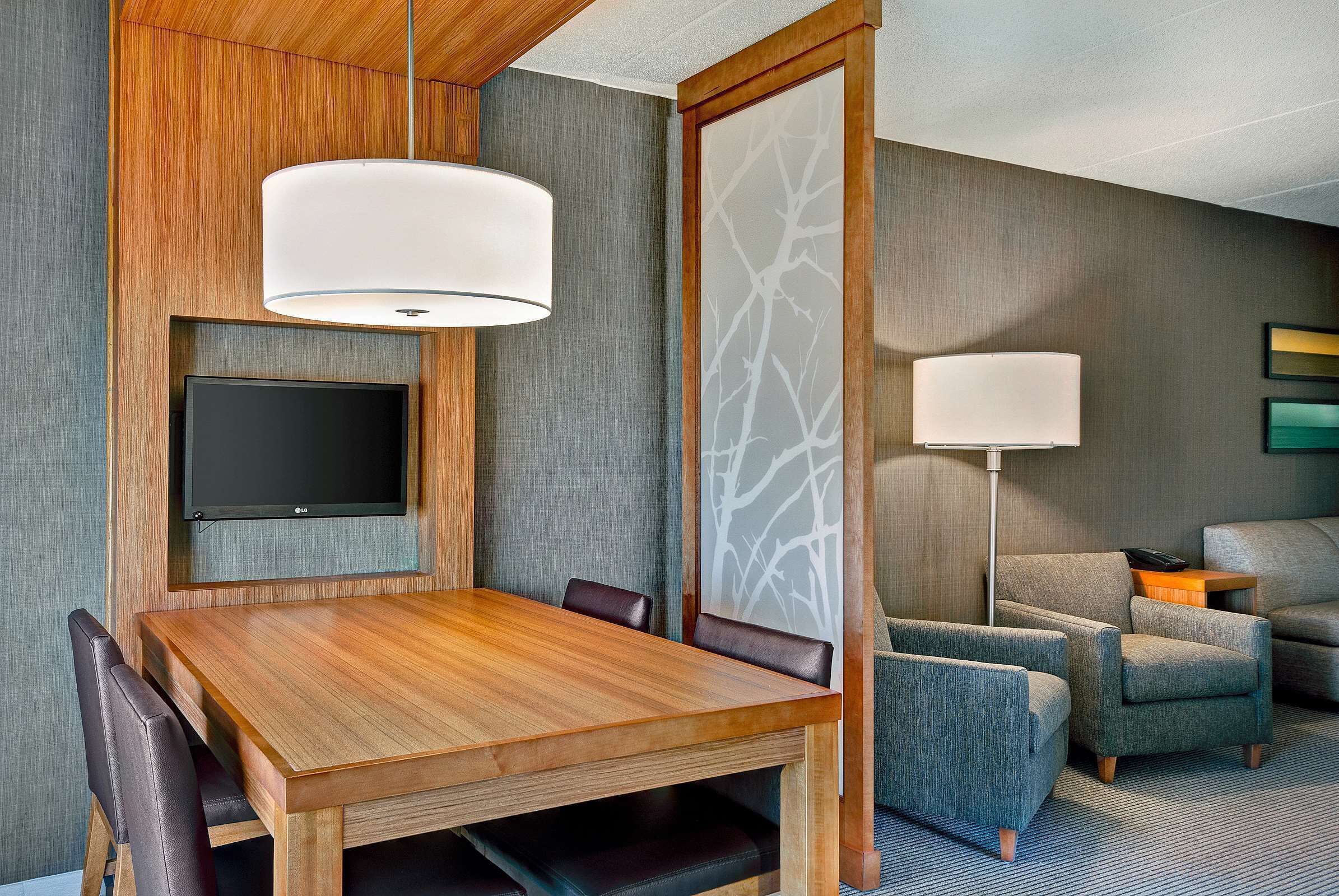 Une chambre d’hôtel moderne dotée d’une table à manger en bois, de sièges confortables, d’un téléviseur à écran plat et d’une grande fenêtre offrant une vue panoramique.