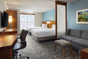 Una habitación de hotel con escritorio, dos camas, sofá y televisión.