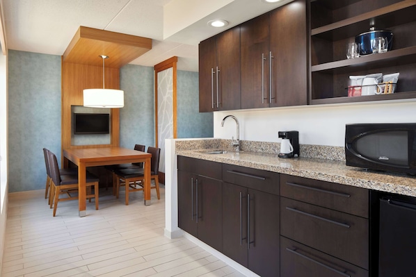 A modern kitchen with dark wood cabinets, a granite countertop, a built-in microwave, and a dining area with a wooden table and chairs.