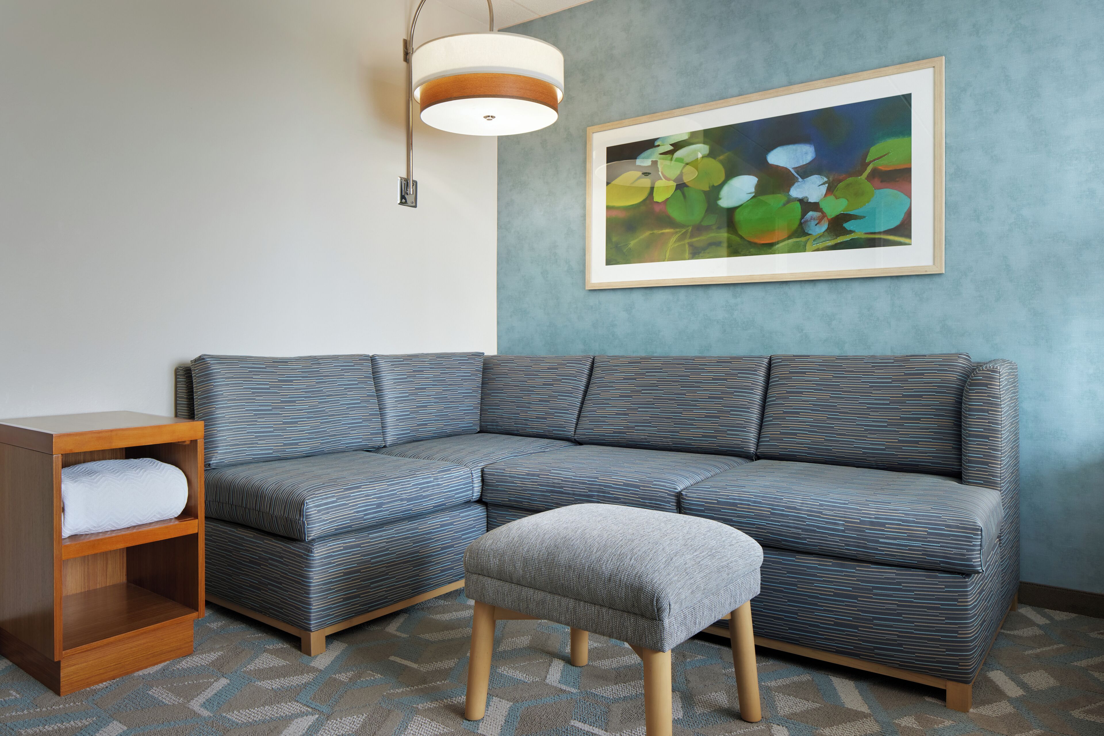 A modern living room with a sectional sofa, a wooden nightstand, and a gray ottoman.
