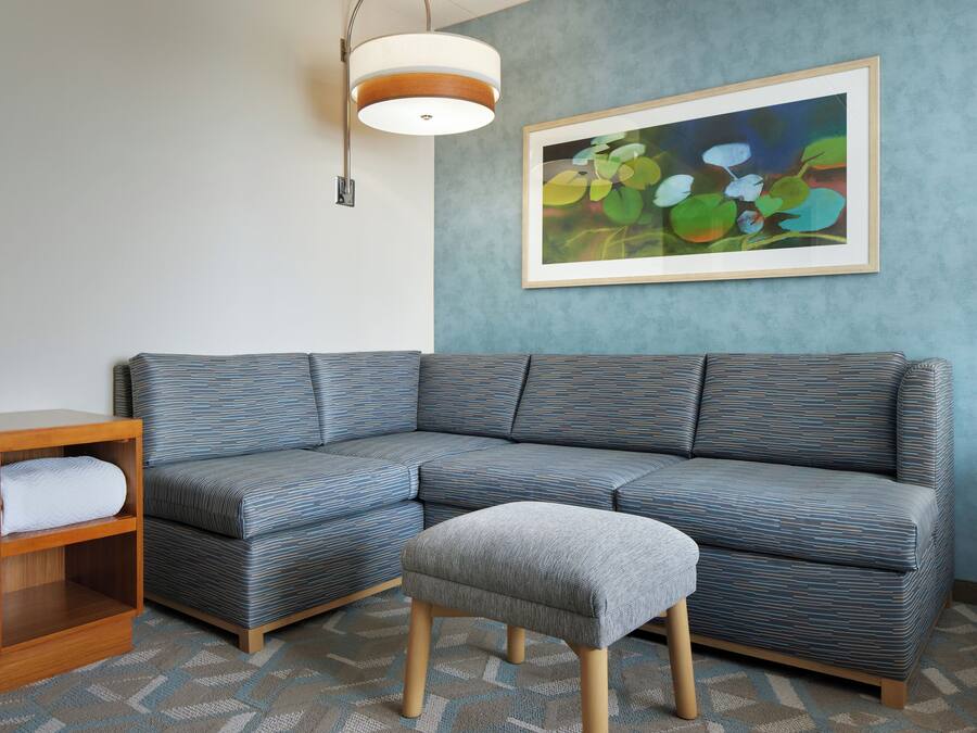 A modern living room with a sectional sofa, a wooden nightstand, and a gray ottoman.