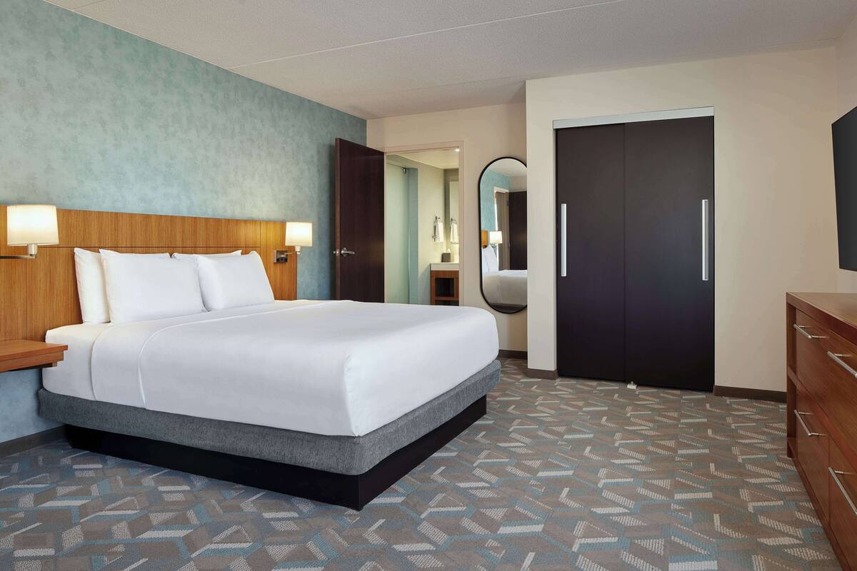 A hotel room with a bed, bedside lamps, a dresser, a mirror, and a door.