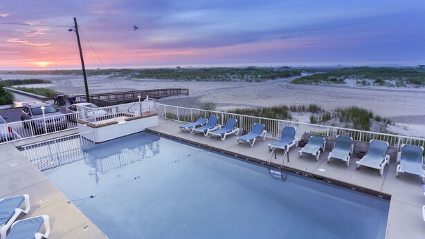 A swimming pool with lounge chairs and a view of the beach at sunset. - Granada Ocean Resort (Wildwood Crest)