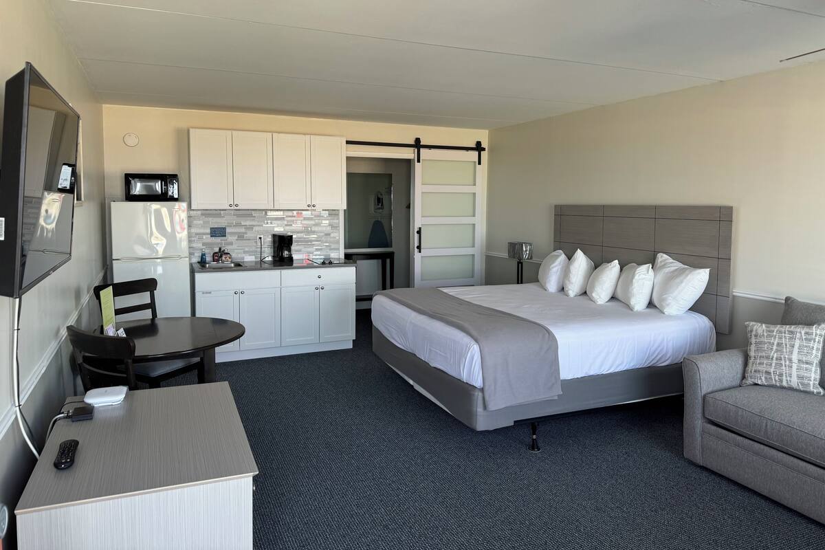 A hotel room with a bed, a desk, a chair, a kitchenette, and a bathroom.