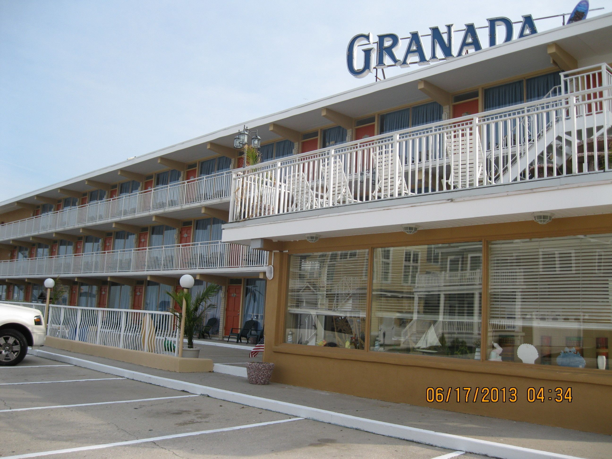 Un hotel con un cartel con el nombre 'GRANADA'. Tiene varios balcones con barandillas, un estacionamiento con un coche blanco y un sello de fecha '06/17/2013 04:34'.