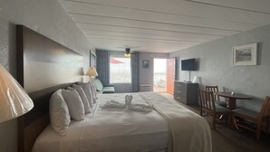 A hotel room with a bed, a desk, a chair, a TV, and a view of the outside. - Granada Ocean Resort (Wildwood Crest)