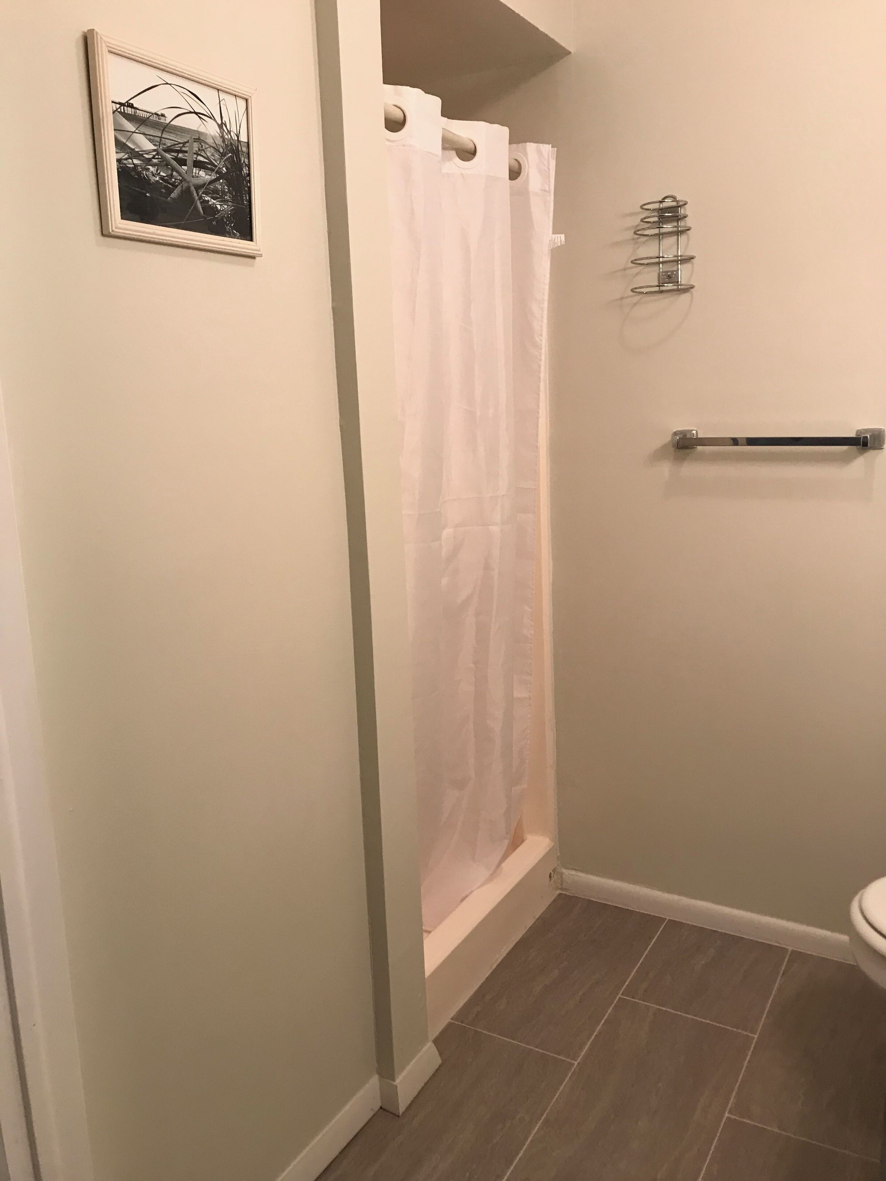 Un baño con cortina de ducha blanca, perchero y un cuadro en la pared.