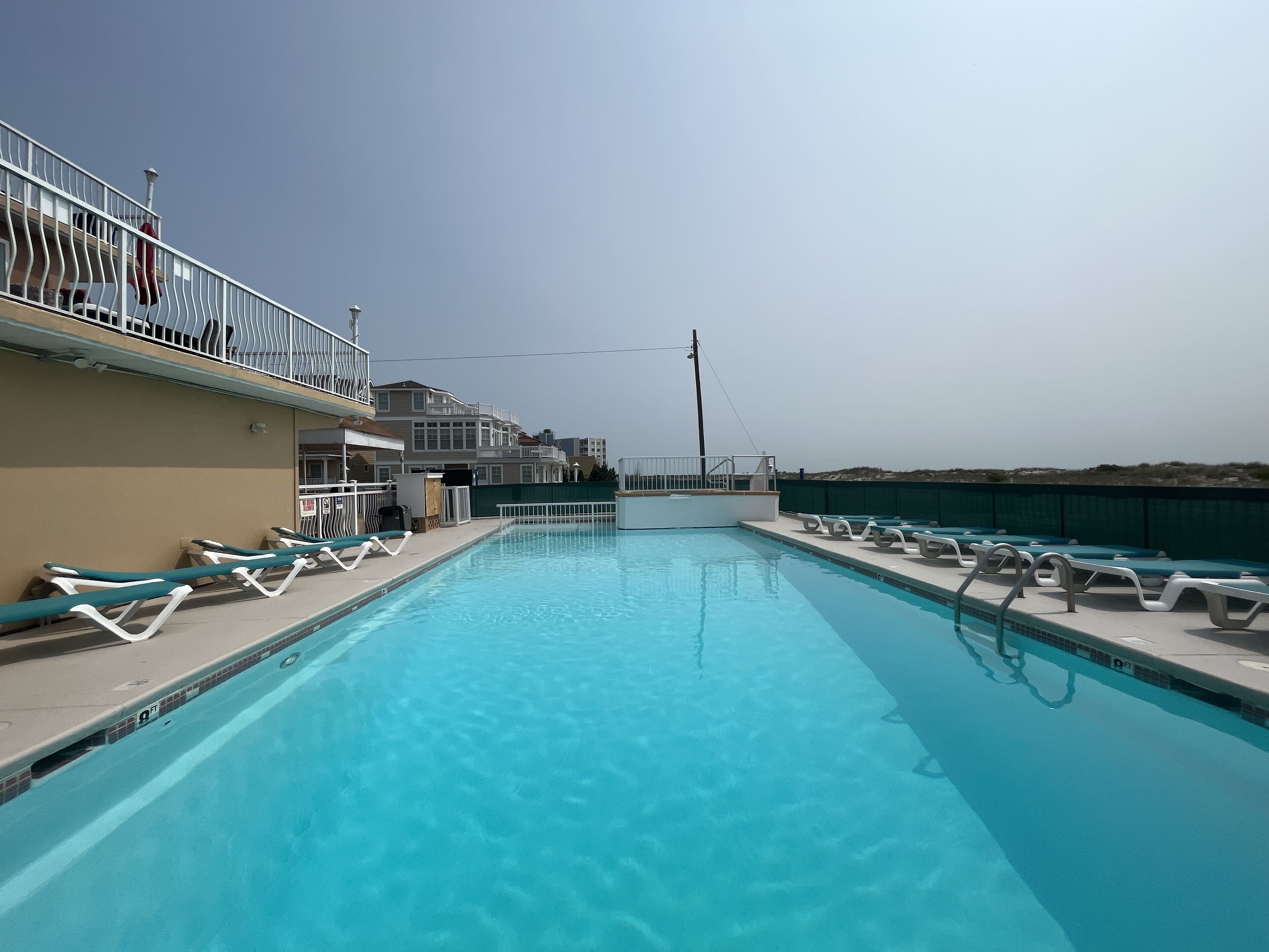 A swimming pool with lounge chairs and a balcony with railings.