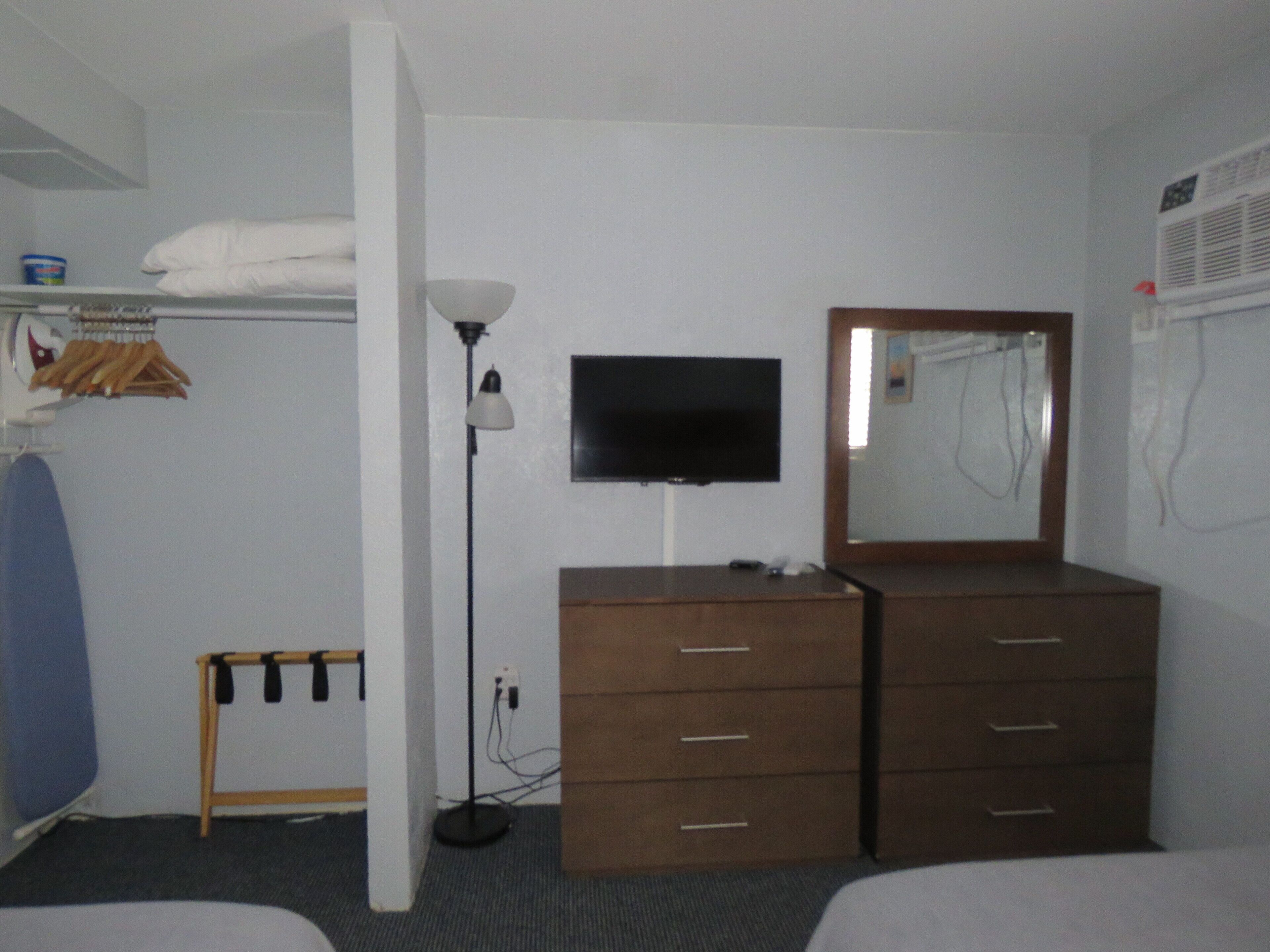A hotel room with a bed, a dresser, a TV, a lamp, and a mirror.