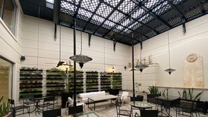 Amplio espacio interior con techos altos, que incluye una zona de estar central con un sofá blanco y varias mesas y sillas.