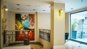 Un lobby moderno de hotel con una escalera, un cuadro abstracto grande y vistas al exterior.
