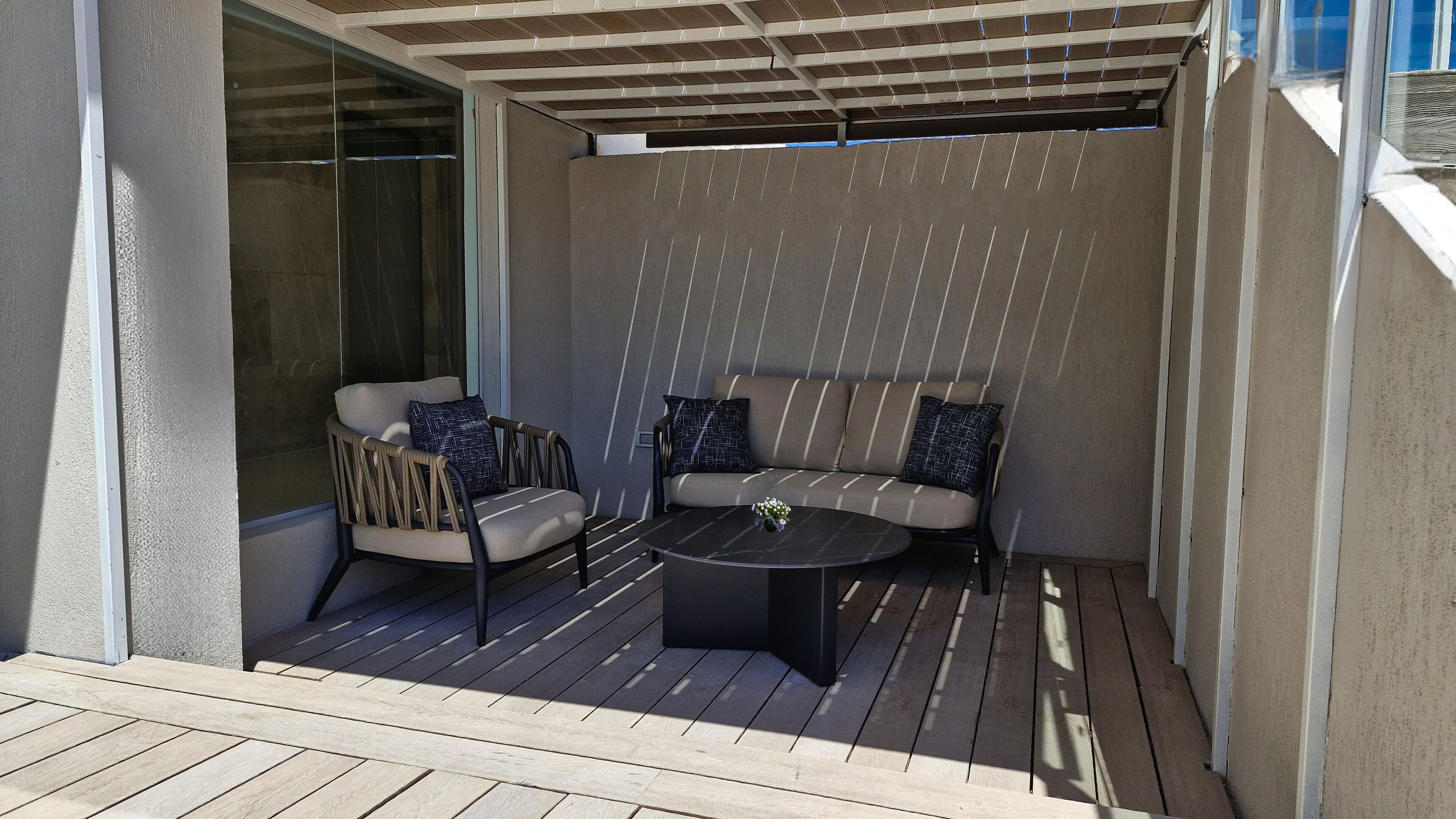 A covered outdoor seating area with a wooden deck, a round table, and two sofas with patterned cushions.
