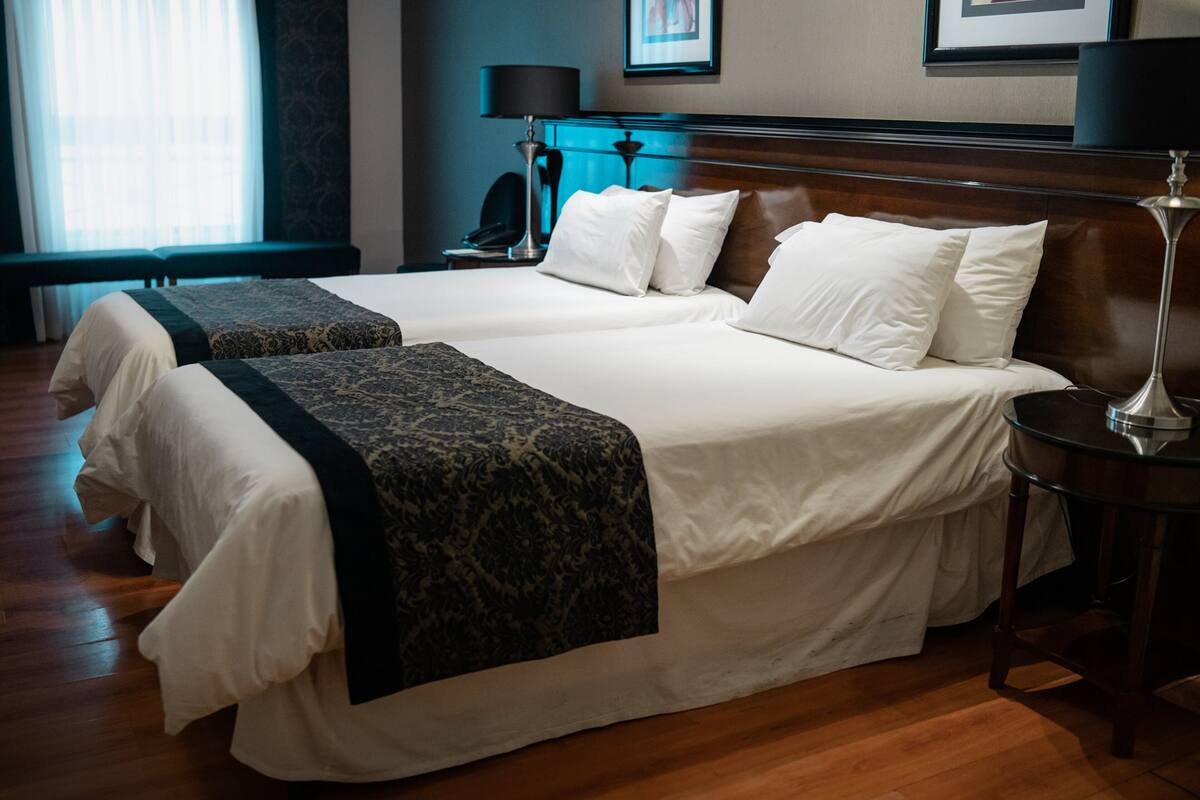 A hotel room with two beds, a bench, a desk, and a lamp.