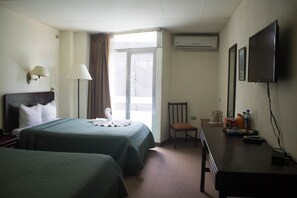 A hotel room with two beds, a desk, a chair, a TV, and a window with curtains. - Hotel El Maragato (San José)