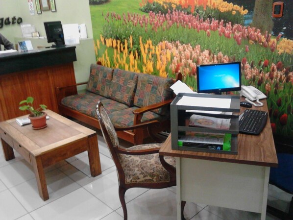 A reception area with a wooden desk, a computer, a telephone, and a sofa. - Hotel El Maragato (San José)