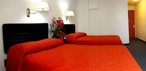 A hotel room with two beds, each with an orange bedspread, a black headboard, and two wall-mounted lamps. - Hotel El Maragato (San José)