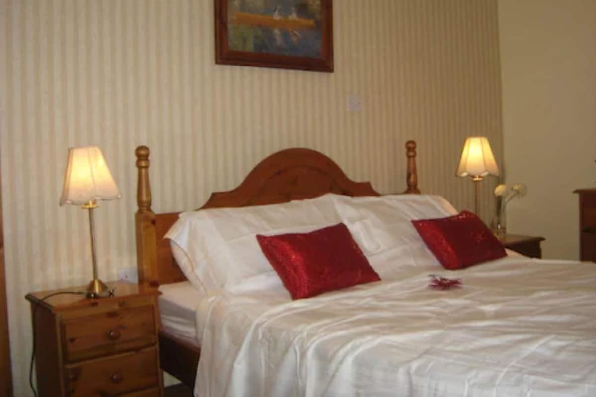 A neatly made bed with white linens and two red pillows, flanked by bedside tables with lamps.